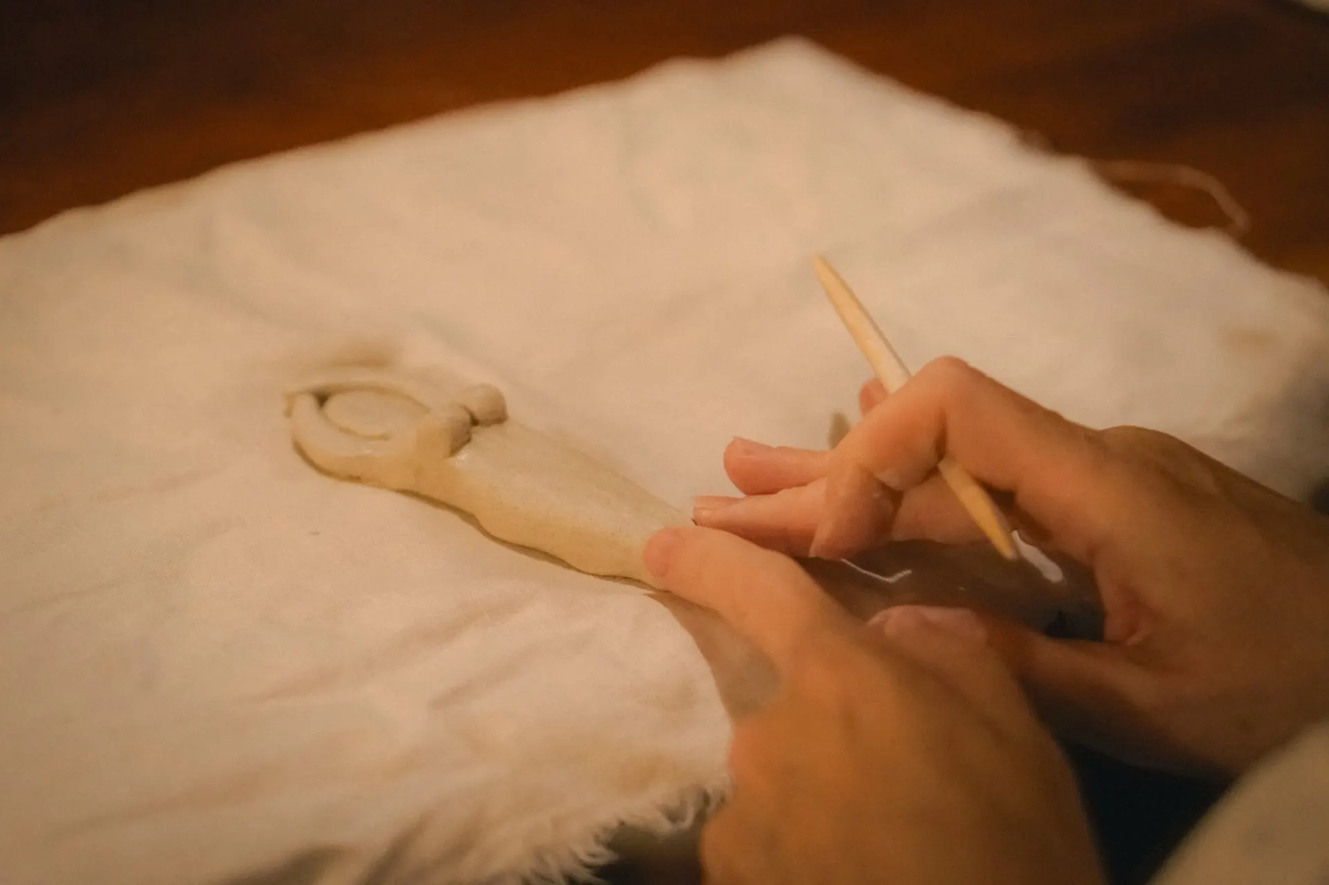 Hands shaping a small clay figure on linen, slow, careful work