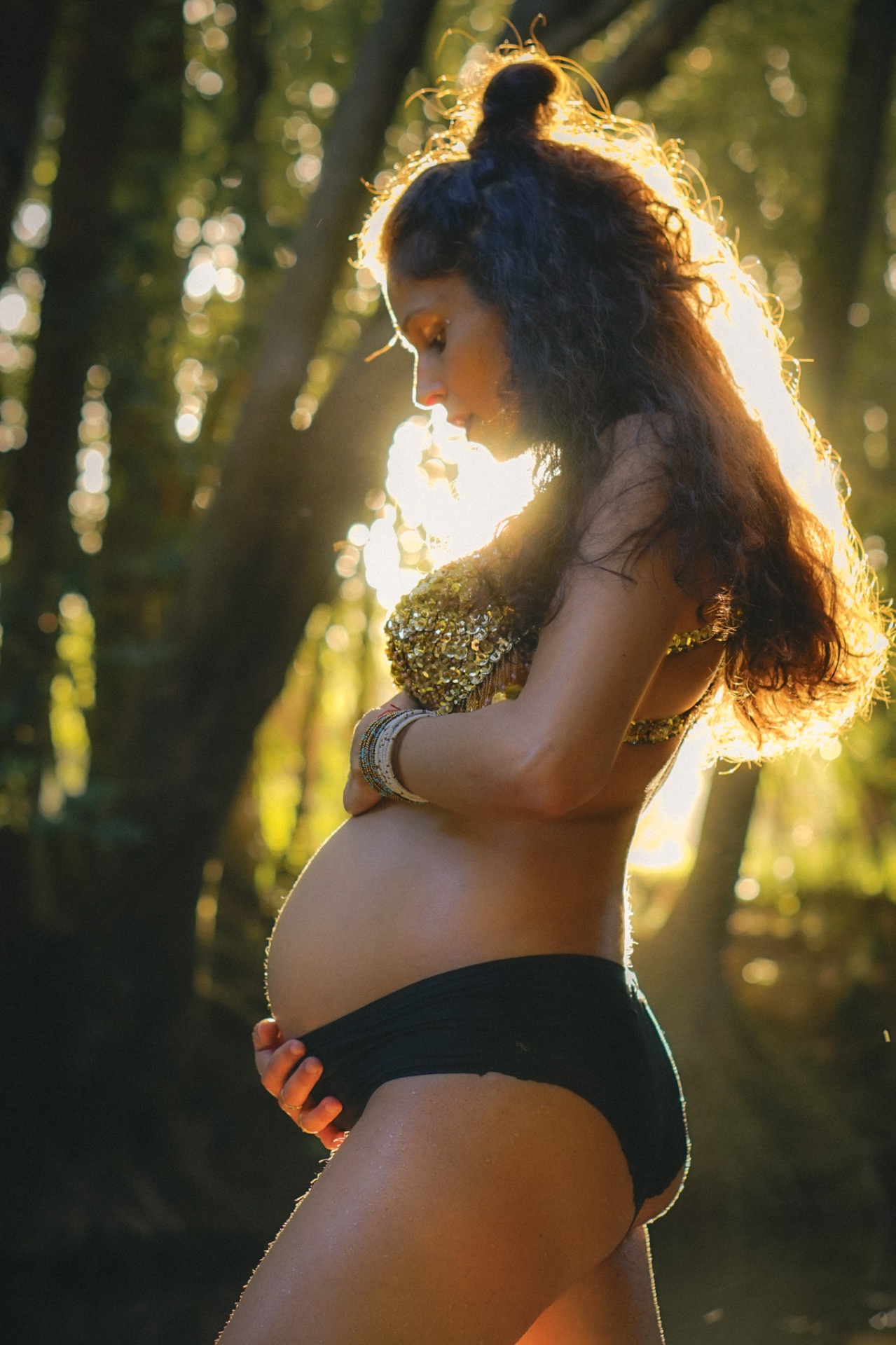 Golden backlit maternity portrait with hands resting on belly