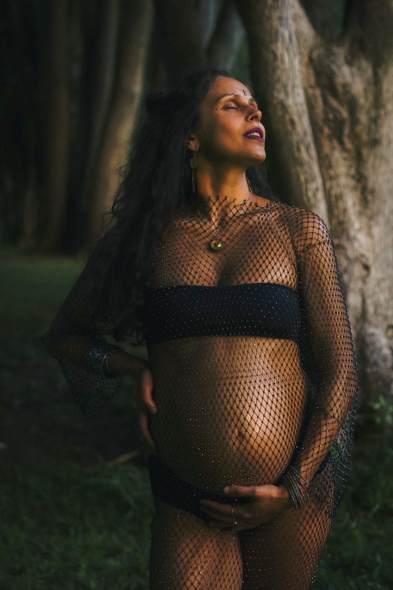 Editorial maternity portrait in dark veil beside trees