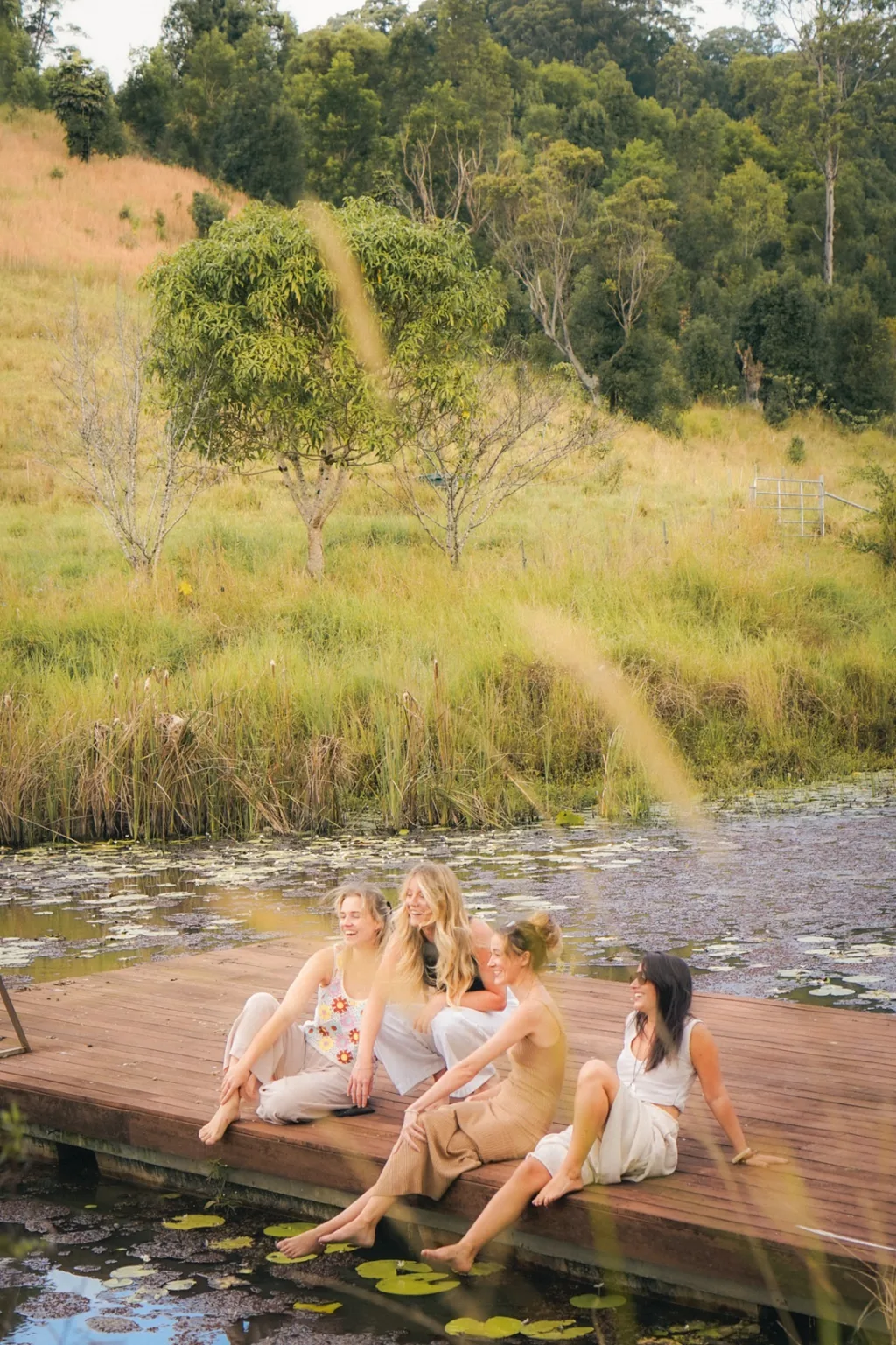 Four women laughing together on a timber dock by a lily-pad pond at Wybalena Organic Farm